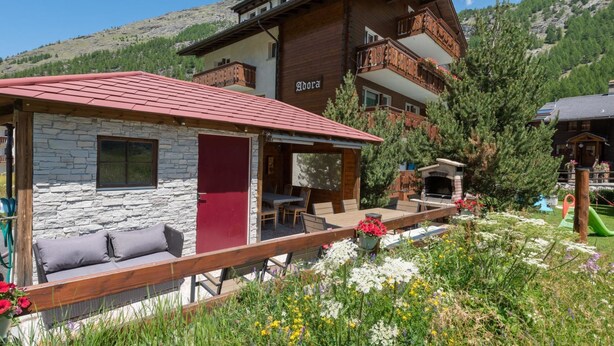 Una baita con facciata in pietra, una porta rossa e un balcone con ringhiere in legno.