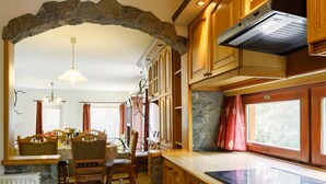 Eine Küche mit Holzschränken, einem Steingewölbe, einem Essbereich mit Stühlen und einem Tisch sowie einem Fenster mit Vorhängen.