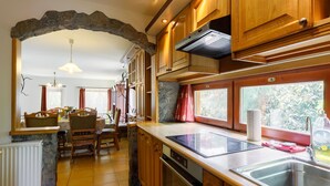 Eine Küche mit Holzausstattung, einem Steingewölbe, einem Essbereich mit Stühlen und Blick durch die Fenster.