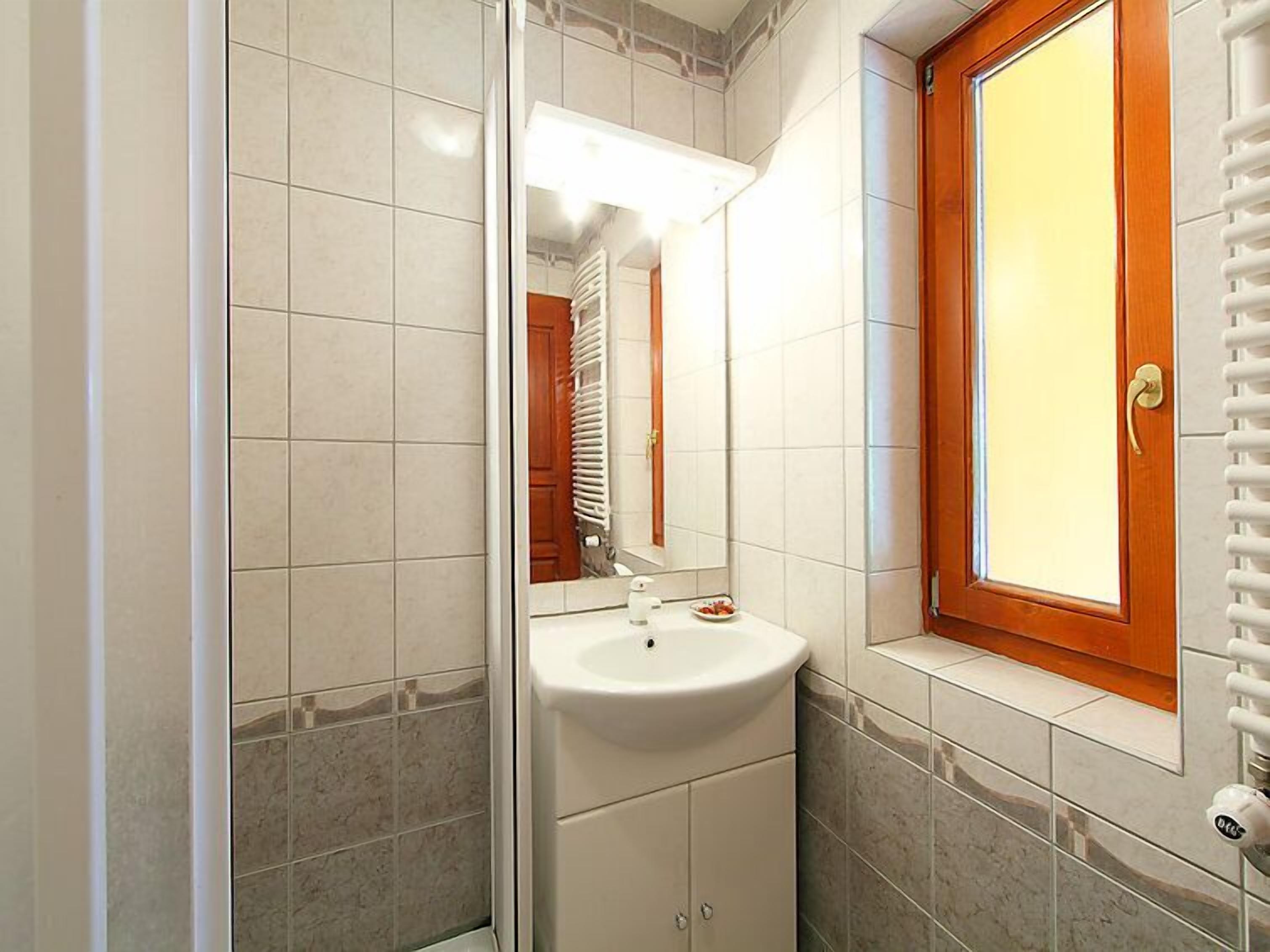 A bathroom with a white sink, a mirror, and a window with a wooden frame.