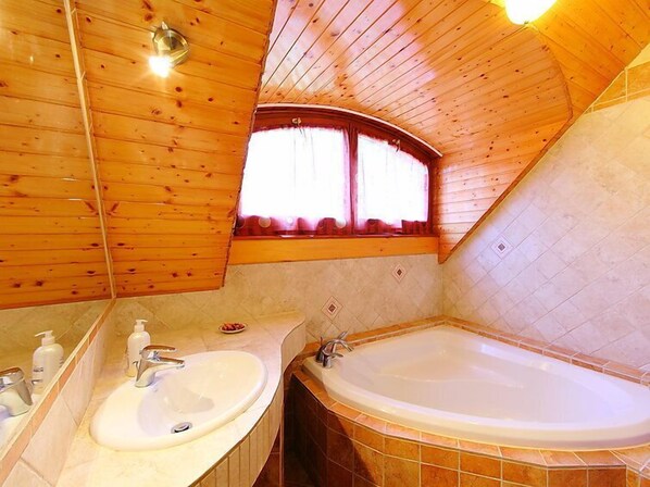 A wooden cabin bathroom with a large bathtub, two sinks, and a window with curtains.