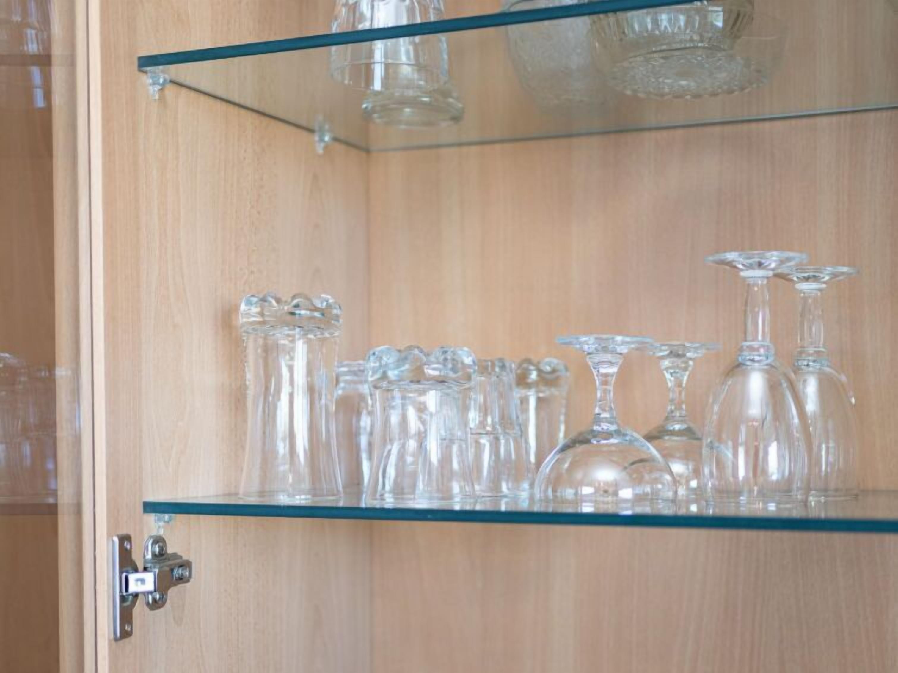 Un meuble en bois doté d’une étagère en verre où sont disposés divers objets en verre transparent.