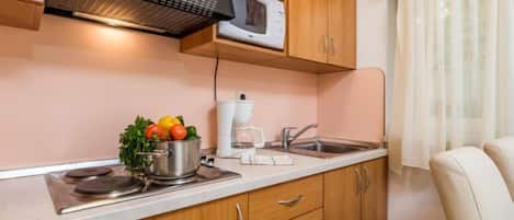 A compact kitchen with wooden cabinets, a microwave, a kettle, and a sink.