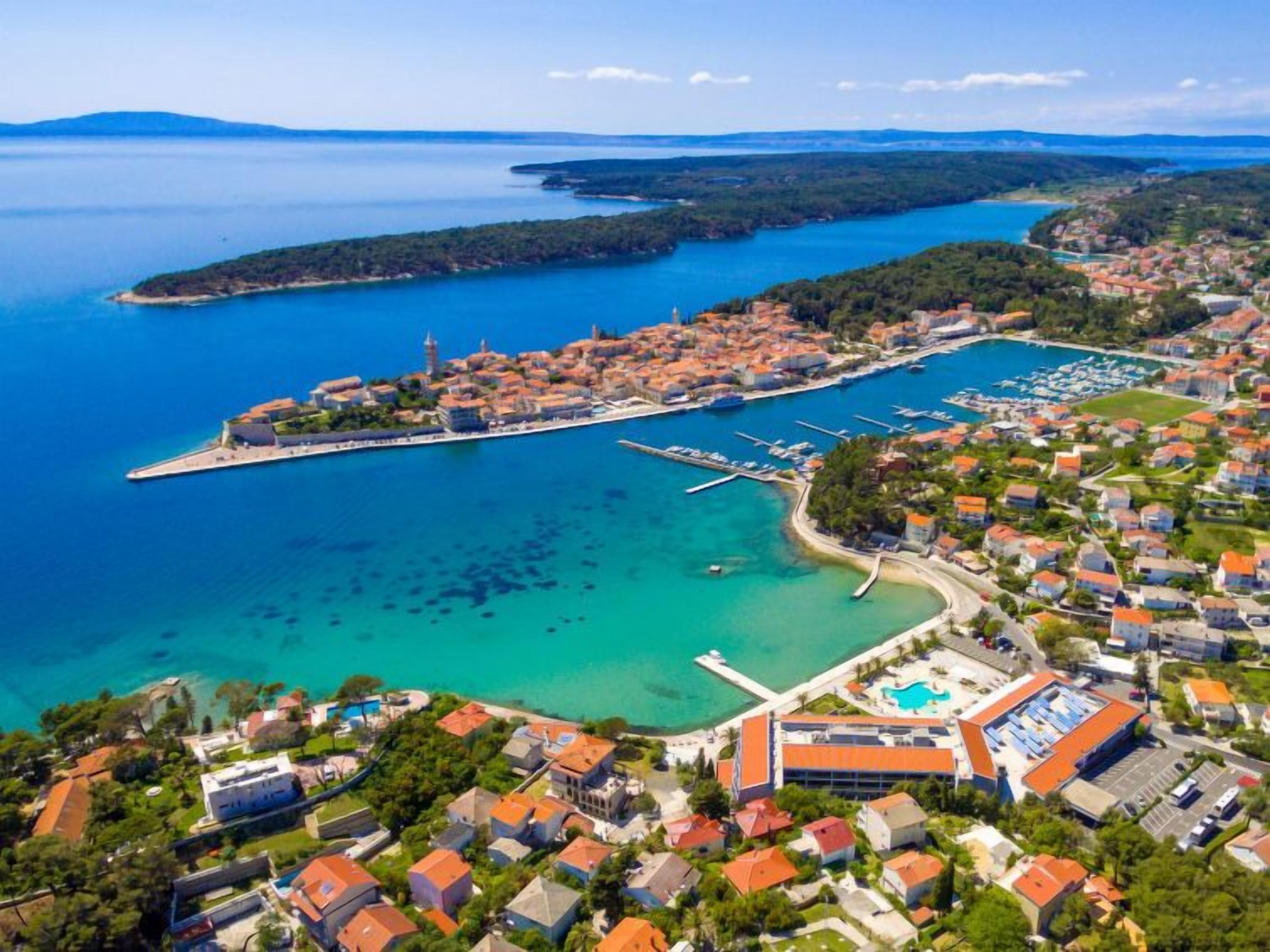 Vue aérienne d’une ville côtière avec un port de plaisance, des immeubles résidentiels et une église imposante.