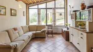 Una sala de estar acogedora con un sofá color beige, techo de madera, un ventanal con cortinas, una mesita con un florero, y un aparador con adornos.