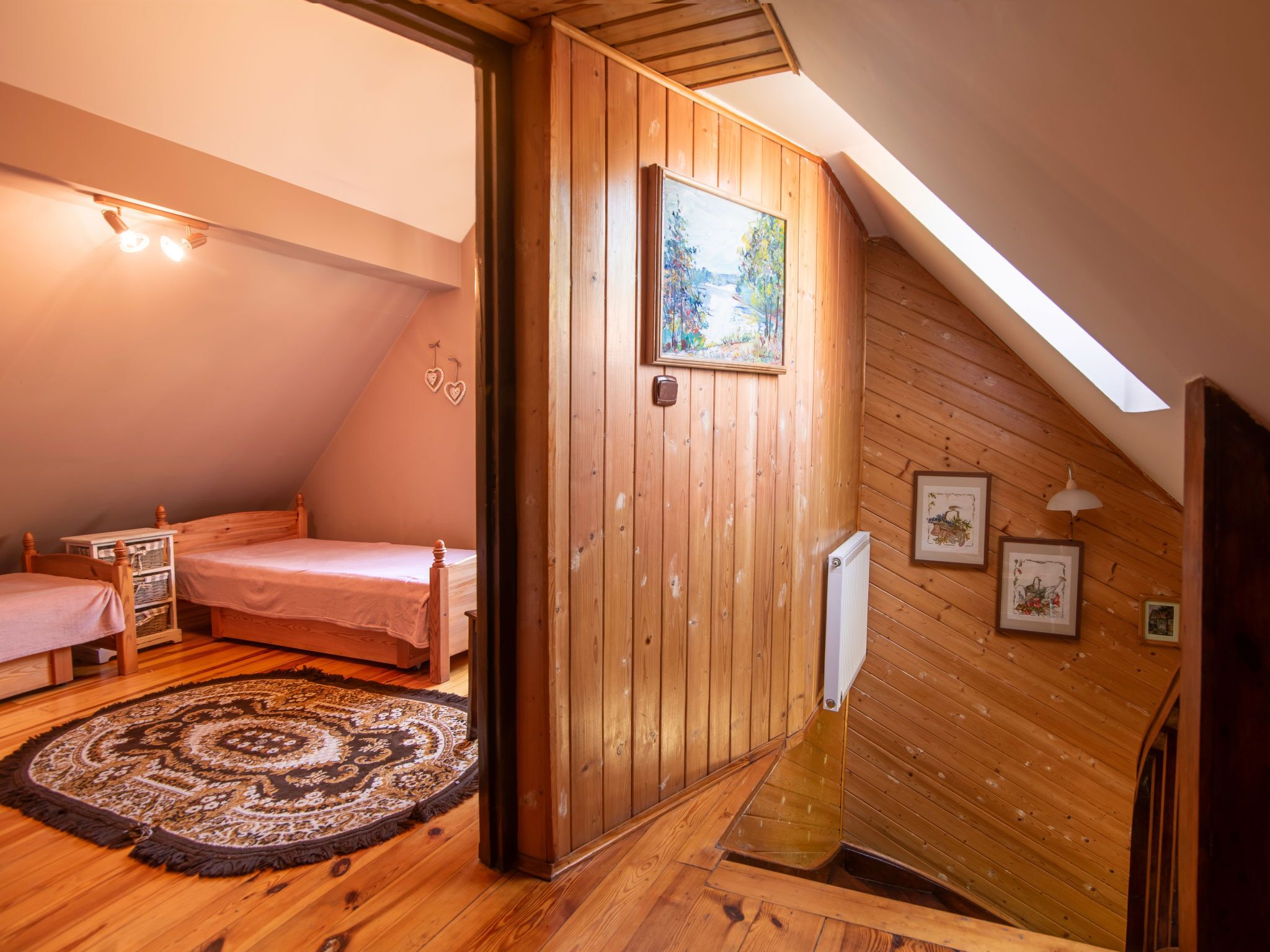 Een knus zolderkamer met houten wanden, een dakraam, een bed, een nachtkastje en een decoratief vloerkleed.