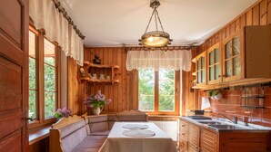 Interior acolhedor de uma cabana de madeira com uma mesa de jantar, bancos e uma área de cozinha.