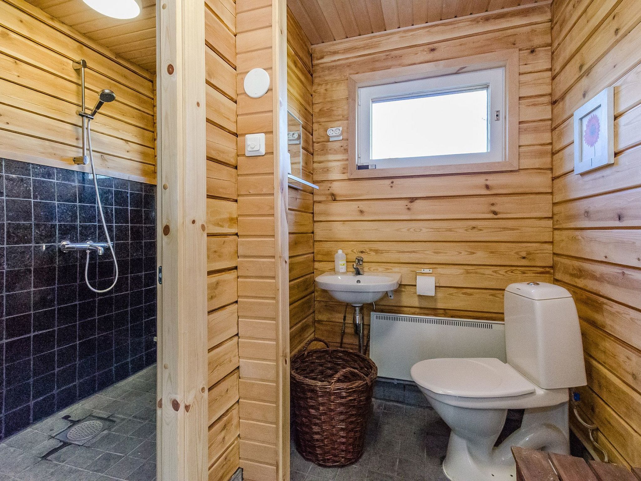 Une salle de bain rustique, aménagée dans une cabane en bois, avec une douche, un lavabo, des toilettes et une fenêtre.