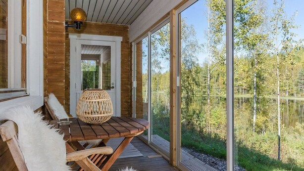 Una terraza de madera con una mesa y sillas, una lámpara de mimbre y vistas a un área boscosa.