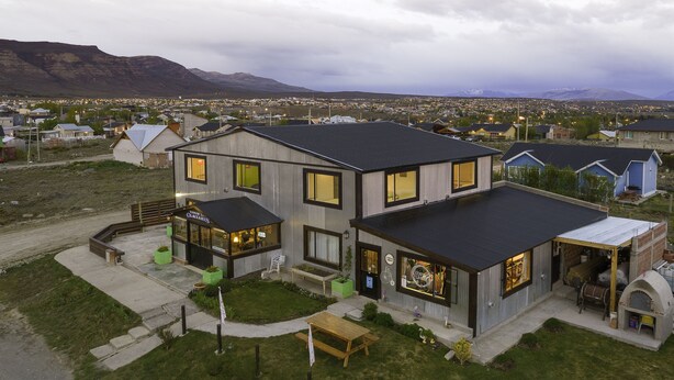 A modern two-story building with a large patio area, a barbecue setup, and a view of a town in the background.
