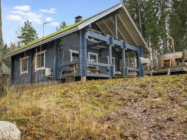 Una casa de madera deteriorada con un techo empinado, rodeada de follaje exuberante y hojas caídas.