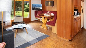 A cozy living room with a dining area, wooden cabinets, a large window with a scenic view, and a mounted TV. - Opale 4 by Interhome (Villars)