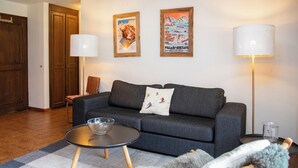 A living room with a dark grey sofa, two framed posters, a glass coffee table, and a lamp. - Opale 4 by Interhome (Villars)