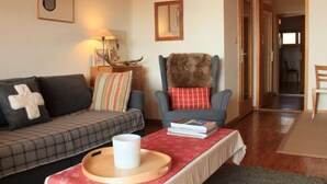 Een gezellige woonkamer met een bank, een fauteuil, een bijzettafeltje met dienblad en een lamp.
