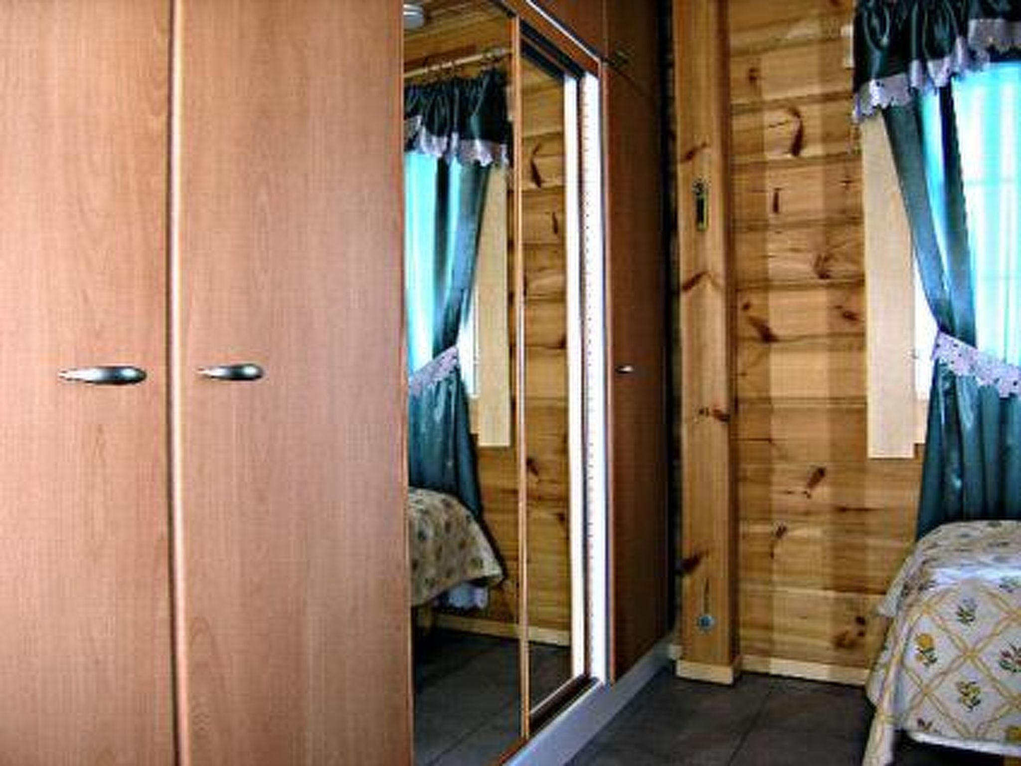 Une pièce en bois avec une porte coulissante, un lit recouvert d’une courtepointe à motifs floraux et une fenêtre avec des rideaux.