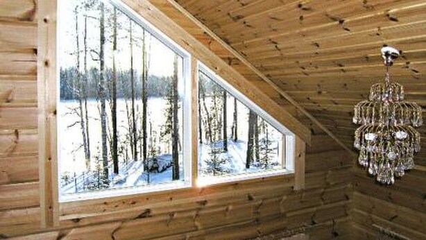 Interior d'una cabana de fusta amb grans finestres que donen vista a un bosc cobert de neu.