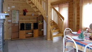 Interior d'una cabana de fusta amb menjador, escala i moble prestatge per a entreteniment.