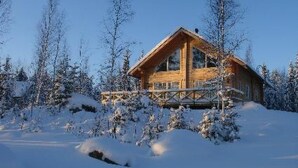 Una cabana de fusta amb un balcó, envoltada d'arbres coberts de neu.
