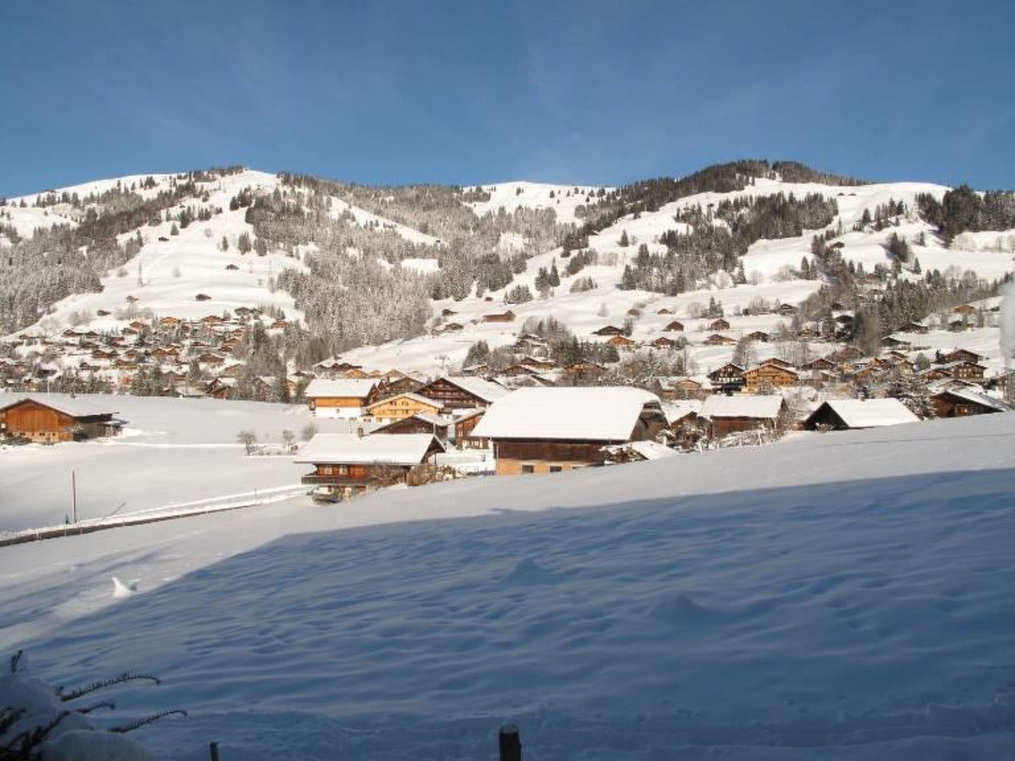 Ein schneebedecktes Dorf mit traditionellen Holzhäusern, blauem Himmel und einem Berg im Hintergrund.