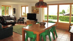 Ein geräumiges Wohnzimmer mit einem Holzespeisetisch, grünen Stühlen, einer Couch und einem Fernseher.