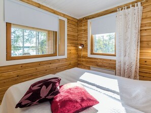 Une pièce de cabane en bois comprenant un lit, deux fenêtres et une vue sur les arbres.