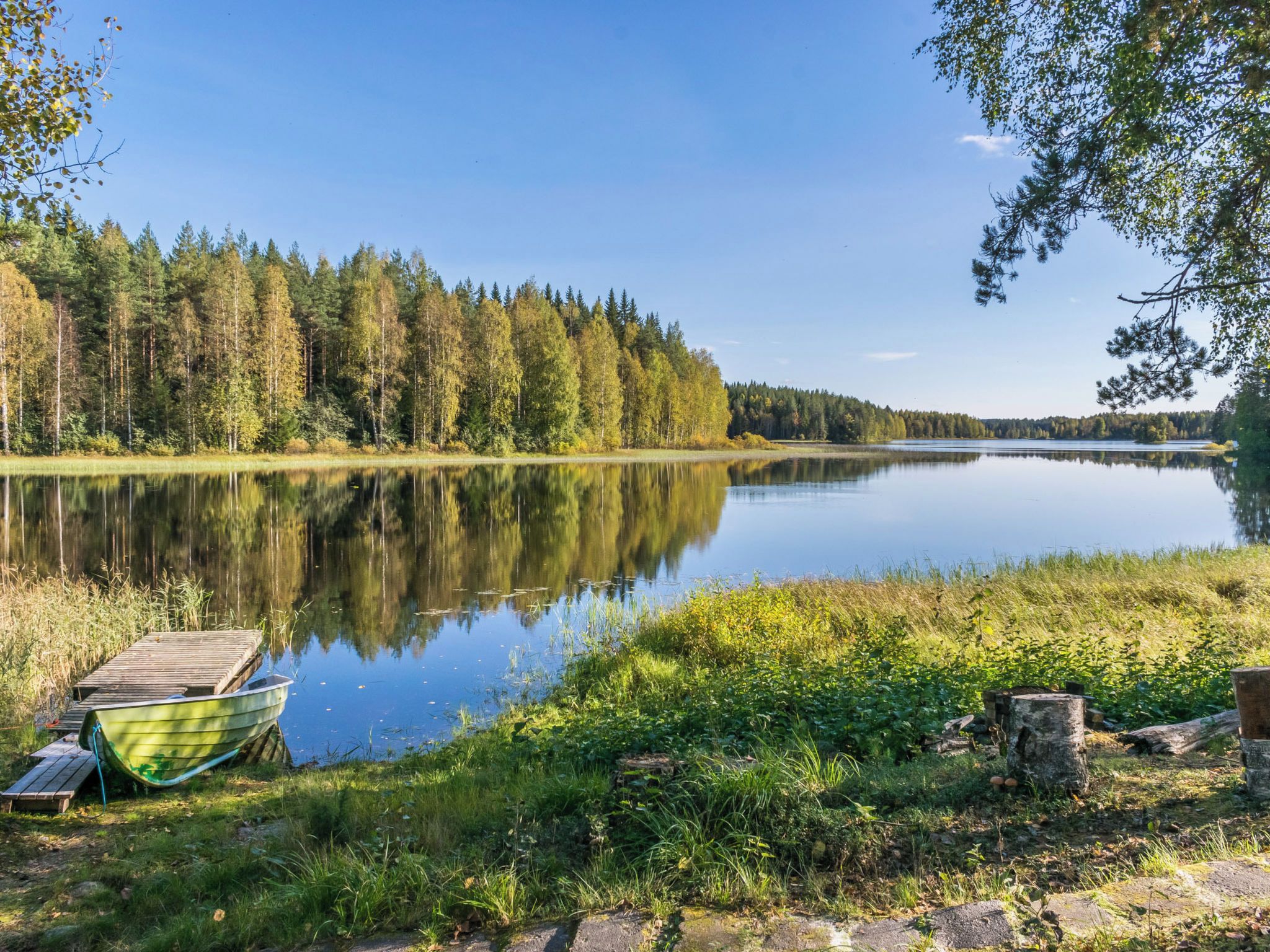En stilla sjö med en brygga och båtar, omgiven av tät skog.
