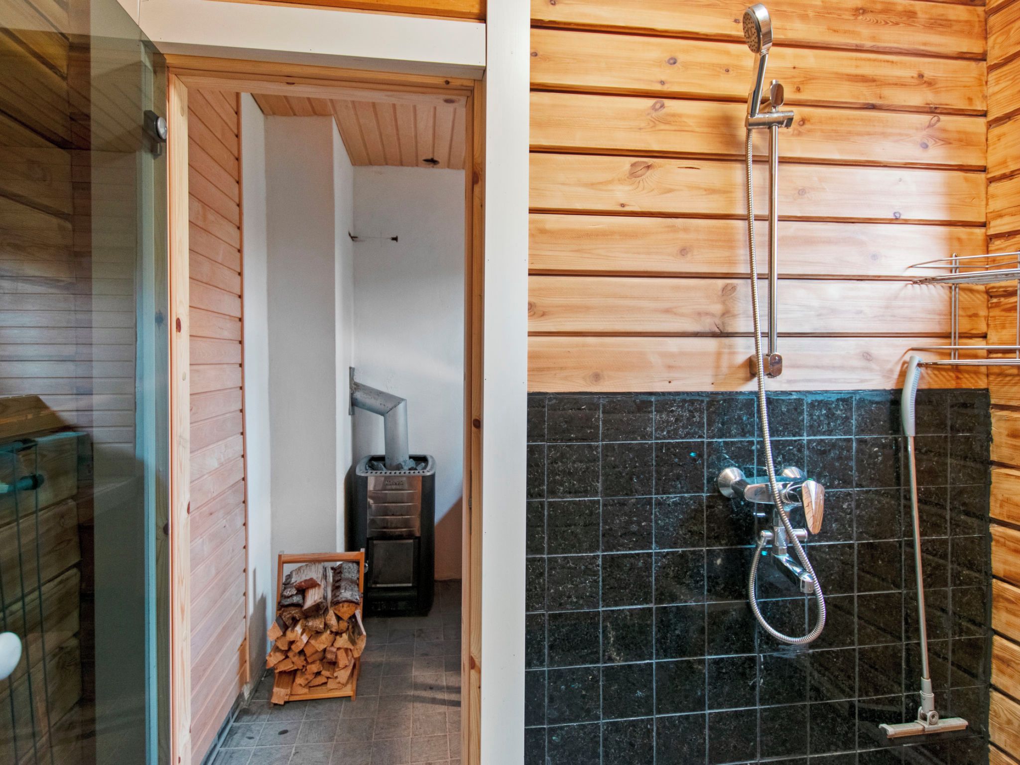 A wooden cabin interior with a shower area featuring a black tiled wall and a metal showerhead.