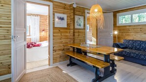 Interior acogedor de una cabaña con detalles de madera, una mesa de comedor con bancos, un sofá y una lámpara colgante.