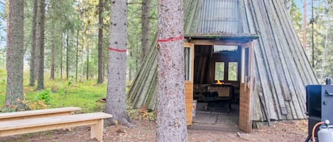 A rustic cabin with a wooden door, a bench, and a fireplace.