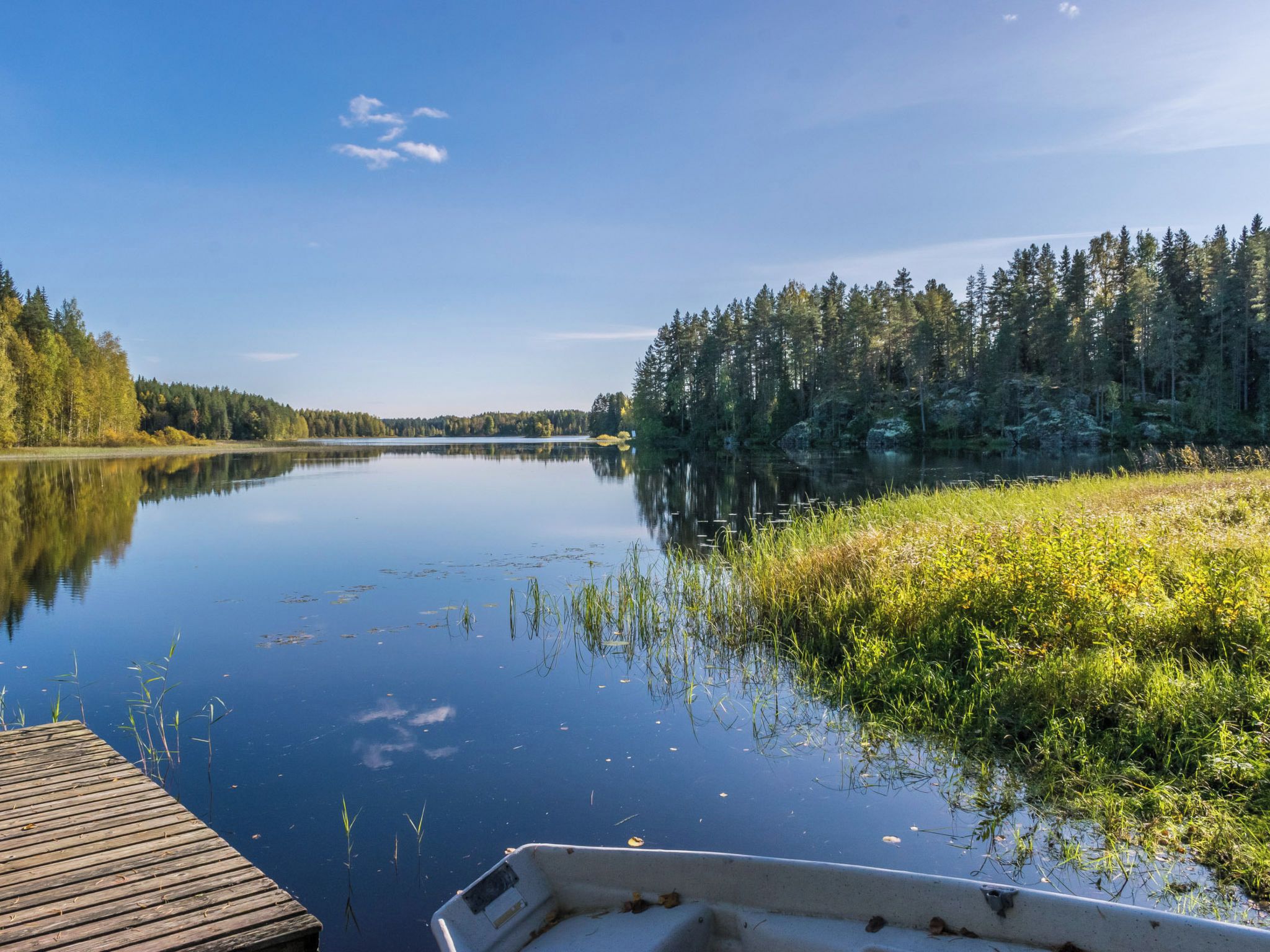 Un lac paisible, avec un quai en bois et un bateau, entouré d’une forêt dense.