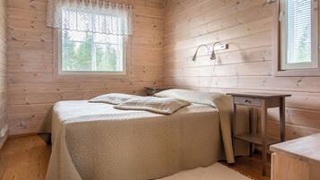 A wooden cabin bedroom with a bed, bedside table, and a window with blinds.