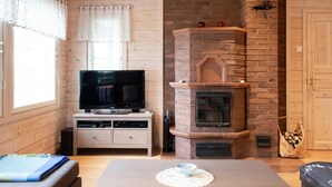 A cozy room with a TV, fireplace, wooden walls, and a window with curtains. - Katajakallio by Interhome (Konnevesi)