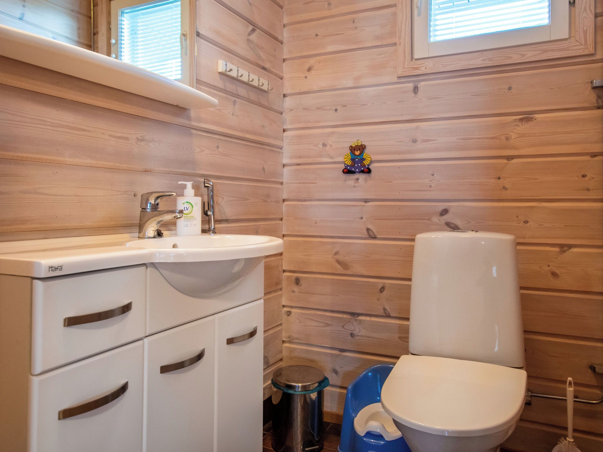 Un baño con paneles de madera, un lavamanos blanco, un inodoro y un cubo de basura.