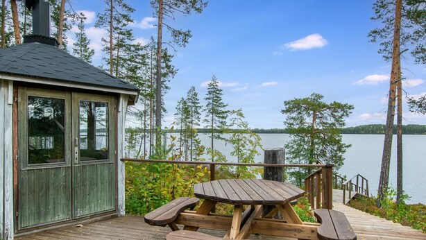 A wooden deck with a picnic table and benches overlooking a lake. - Katajakallio by Interhome (Konnevesi)