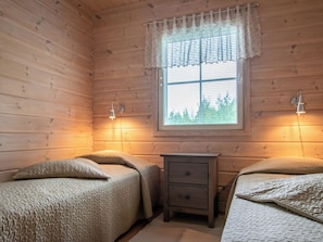 Een kamer met twee bedden, een klein houten nachtkastje en een raam met gordijn.