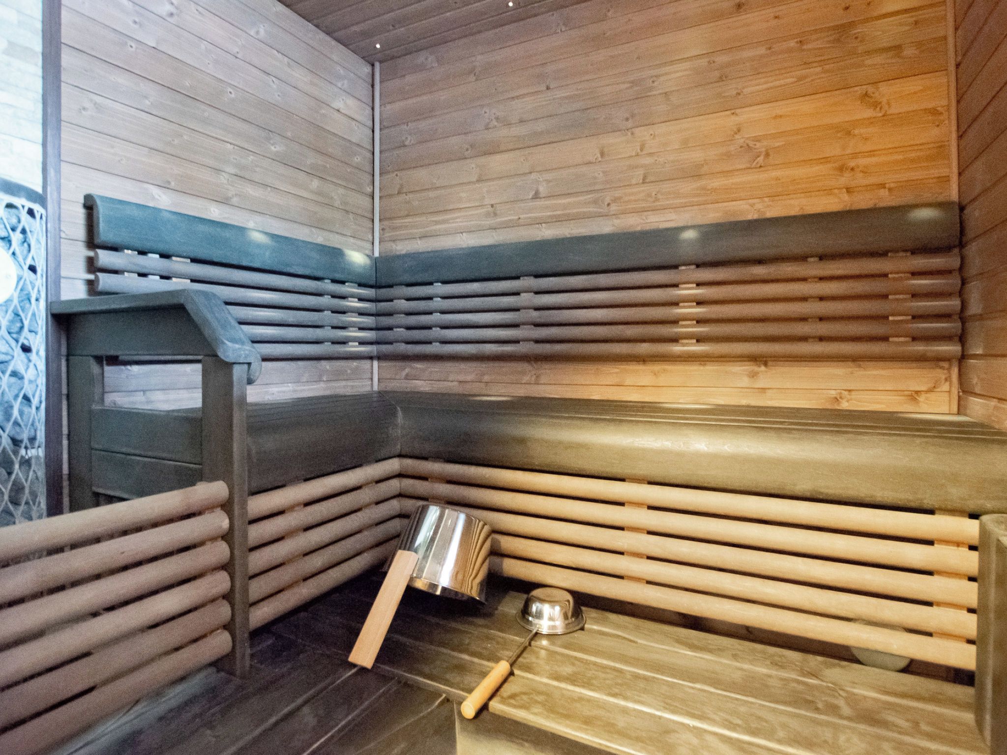 Un sauna avec des bancs en bois et un seau en métal.
