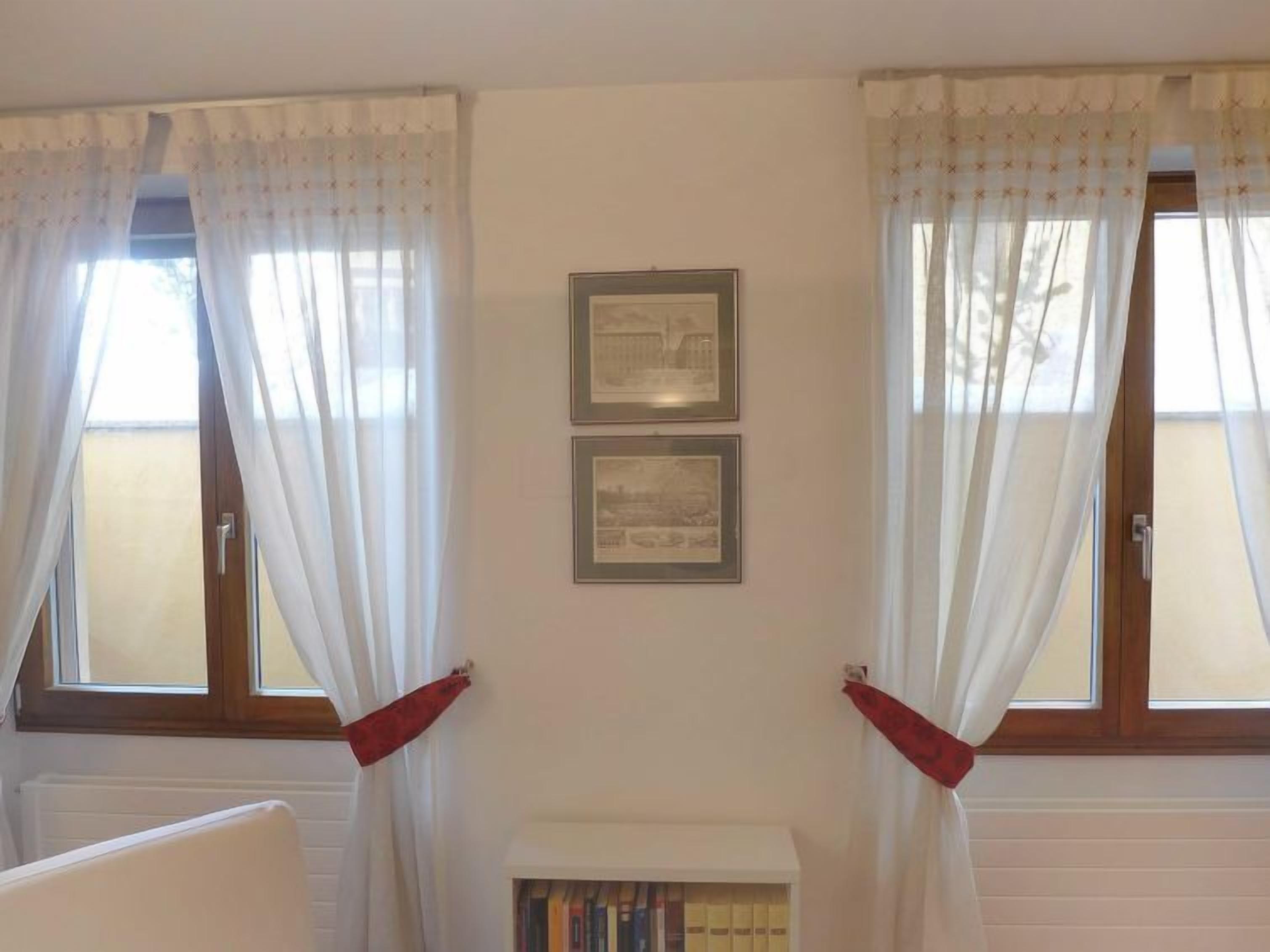 Une pièce avec deux fenêtres, des rideaux blancs et deux tableaux encadrés accrochés au mur.