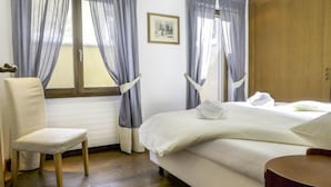 Una habitación de hotel con cama, una silla, un armario de madera y una ventana con cortinas.