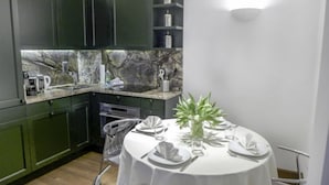 Una cocina compacta con armarios verde oscuro, un salpicadero de mármol y un comedor preparado para cuatro, con mantel blanco y un jarrón con flores.