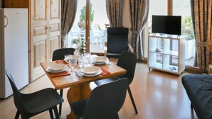 Ein Essbereich mit einem Holztisch, gedeckt für vier Personen, schwarzen Stühlen, einem Fernseher auf einem Schrank und Blick ins Freie durch große Fenster.