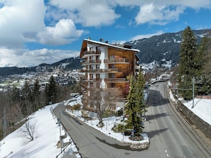 Un edificio de varios pisos con balcones, un paisaje nevado y montañas al fondo.