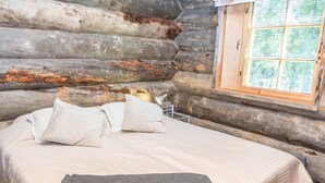 Une chambre aménagée dans un chalet en rondins, avec un lit, des oreillers et une fenêtre donnant sur la forêt.