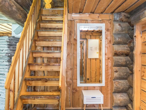 A wooden staircase leading to a log cabin interior with a small white desk and a framed mirror.