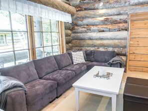 A log cabin interior with a gray sectional sofa, a white coffee table, and a wooden cabinet.