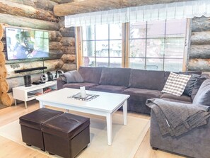 Interior de una cabaña de troncos con televisor, sofá, mesa de centro y reposapiés.