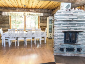 A dining area with a wooden table and chairs, a stone fireplace, and a wooden ceiling. - Costa ruca by Interhome (Kuusamo)