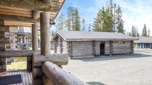 Une cabane rustique en rondins de bois, dotée d’une terrasse en bois et d’une allée gravillonnée.