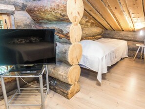 A cozy room with a bed, a television on a stand, and a wooden log wall.