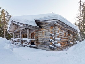 A log cabin with a snow-covered roof, wooden exterior, and a front porch.