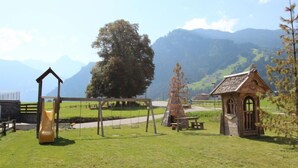 A playground with a swing set and a slide, a picnic table, and a small wooden structure, set against a backdrop of mountains and a clear sky. - Schwendau by Interhome (Mayrhofen)